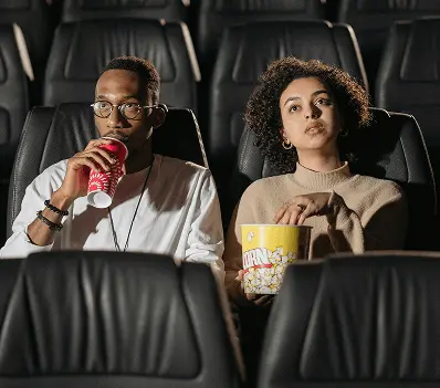 A couple sitting in the cinema sipping an ice cold beverage and snacking on popcorn.